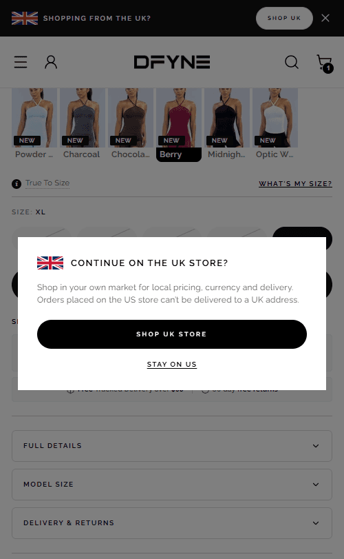 The US store on a phone with a card over it reading 'Continue on the UK store?' — 'Shop in your own market for local pricing, currency and delivery. Orders placed on the US store can't be delivered to a UK address.' — above a 'Shop UK store' button and a 'Stay on US' link. A bar pinned to the top of the page asks the same thing.